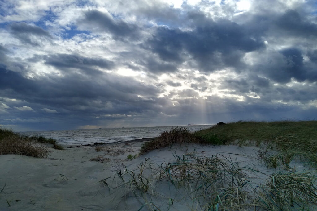 Dunkle unheilvolle Wolken am Nordseestrand mit Sonnenstrahlen im Hintergrund - Naturing Myself - Bindungstrauma und Wut im Erwachsenenalter